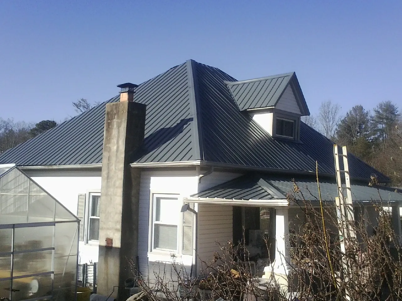 Dark blue standing seam metal roof on a white farmhouse with dormer — Slate & Tile Roof Repair by Roofing Brothers in Algonquin