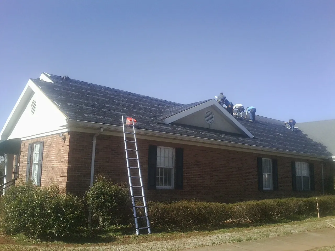 Crew tearing shingles off a brick ranch roof with a ladder set — Emergency Roof Repair work by our crew in Algonquin