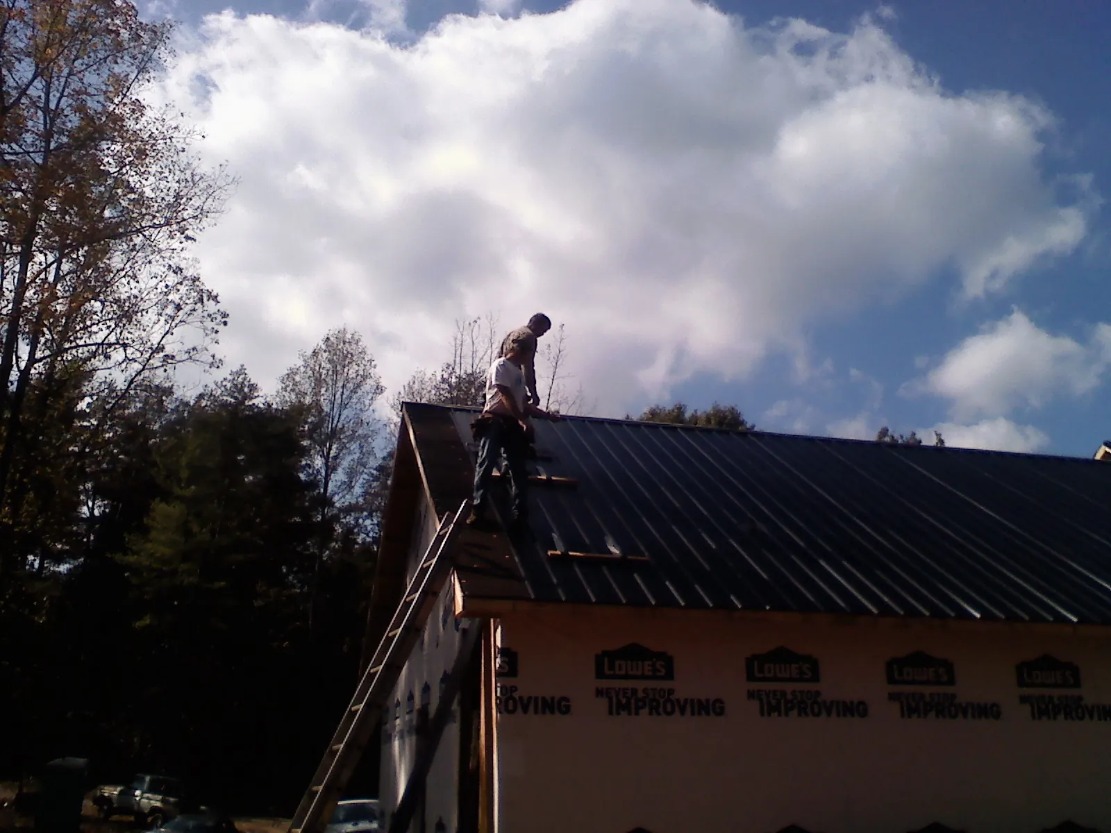 Roofer fastening dark metal panels high against a cloudy sky, from a Roof Inspection job in Algonquin
