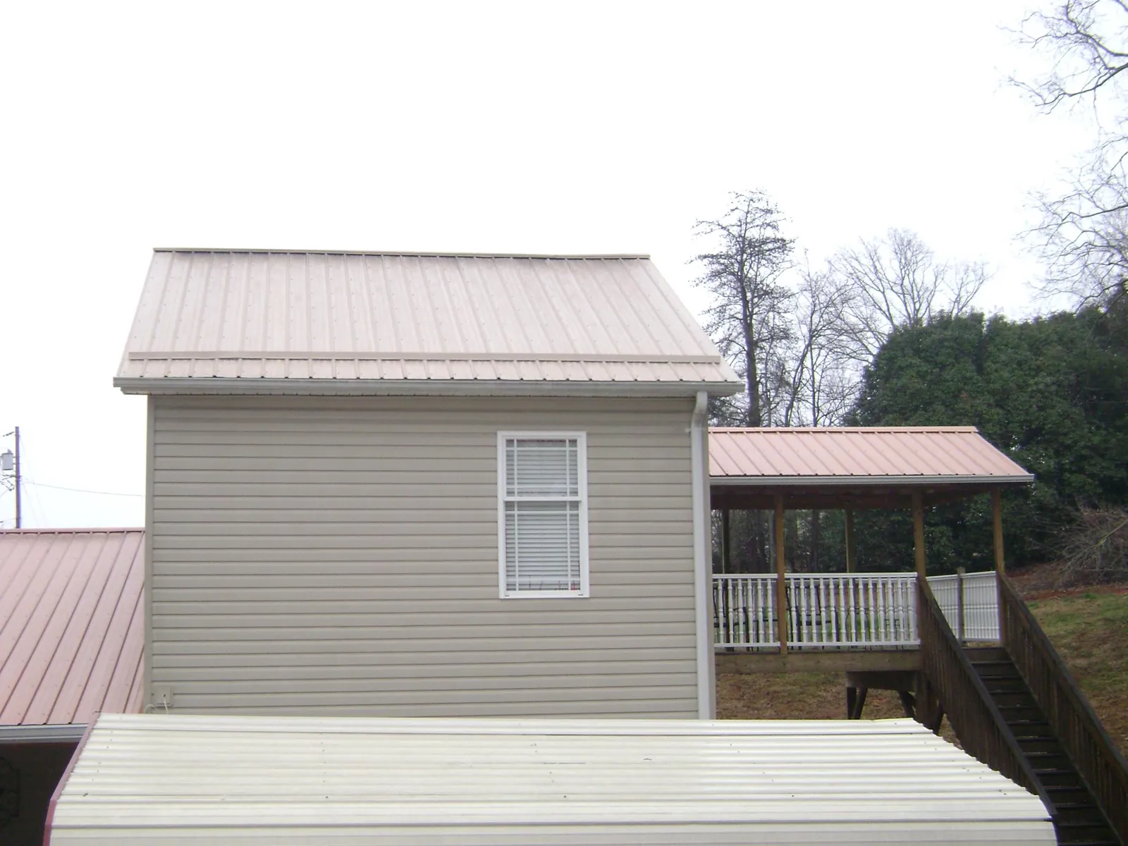 Tan metal roofs on a two story addition and attached porch, from a Roof Replacement job in Algonquin